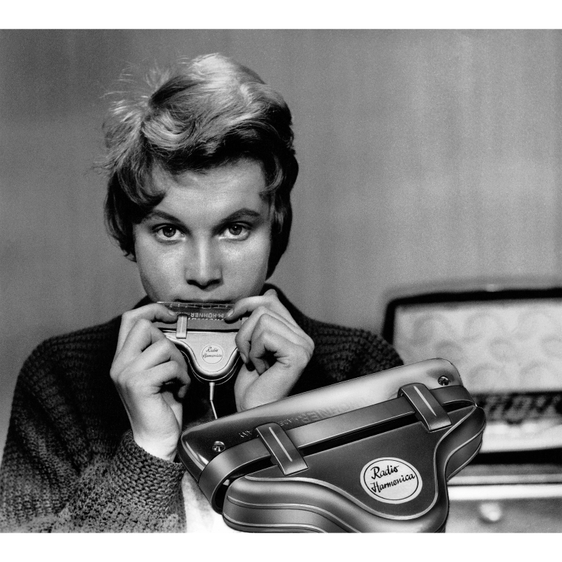 Schwarz weiß Werbefoto für das peiker Radio Harmonica zeigt eine junge Frau die die Harmonica an ihre Lippen hält, im Vordergrund noch einmal die Harmonica in Groß abgebildet.
