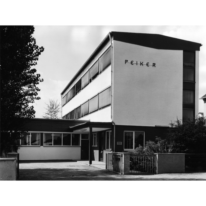 Schwarz Weiß Fotografie des Firmengebäudes, auf der einen Seite steht der Schriftzug PEIKER
