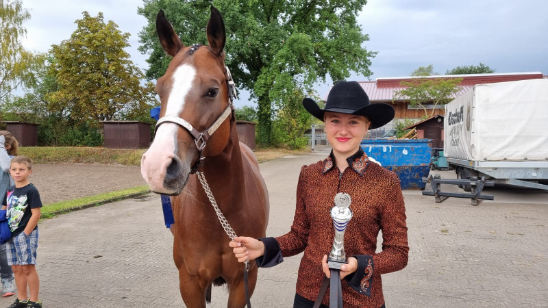 Zoe Knöß stehend neben ihrem Pferd FX Pobrecita Gun mit Pokal