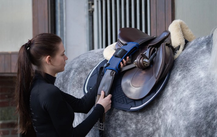 peiker CEE - Frau steht vor einem Pferd mit Sattelgurt in der Hand CEEFIT Pulse ECG Elektrodengurt und CEEFIT Sensor